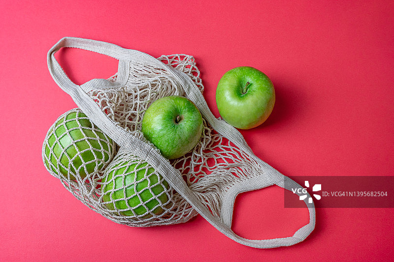 红色背景下棉网购物袋中的有机青苹果图片素材