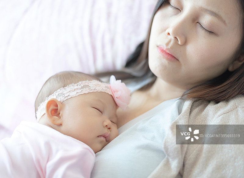 亚洲母亲和婴儿在她怀里，拥抱睡觉。女儿闭上眼睛在母亲的手上睡觉。爱的触摸和家庭关系。生活方式母亲节概念。图片素材