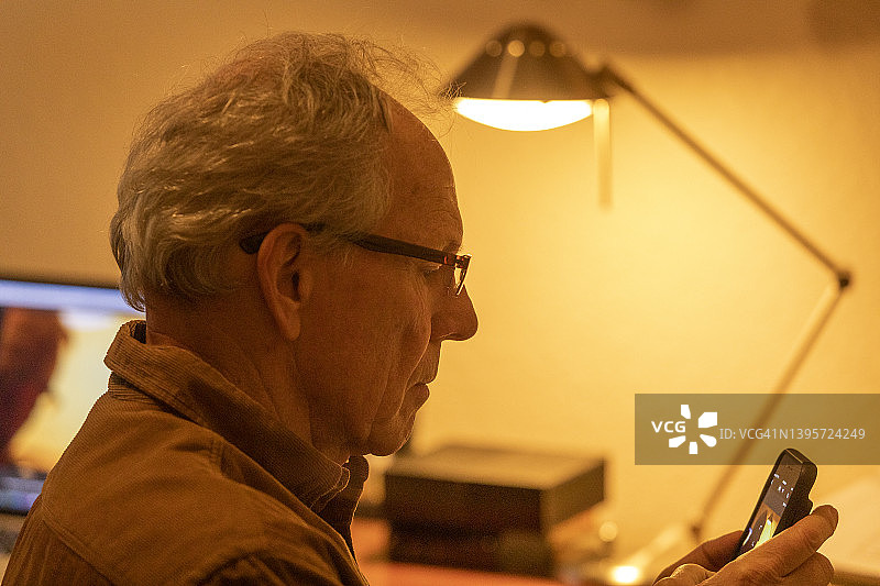 在桌子旁使用智能手机的老年男人侧写图片素材
