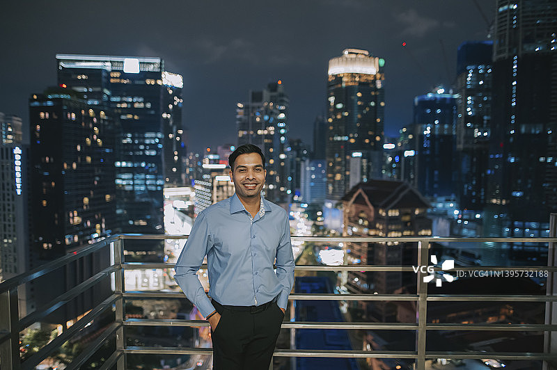 在办公楼外休息的亚裔白领男士，夜晚对着镜头微笑图片素材