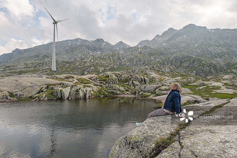高山湖畔风力发电机旁休闲的女人图片素材