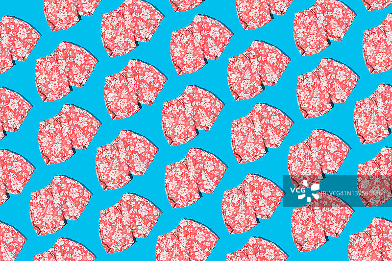 浅蓝色背景上带有树叶和白色花朵图案的粉色男士泳裤，具有硬阴影。关于炎热、夏季和阳光的概念图片素材