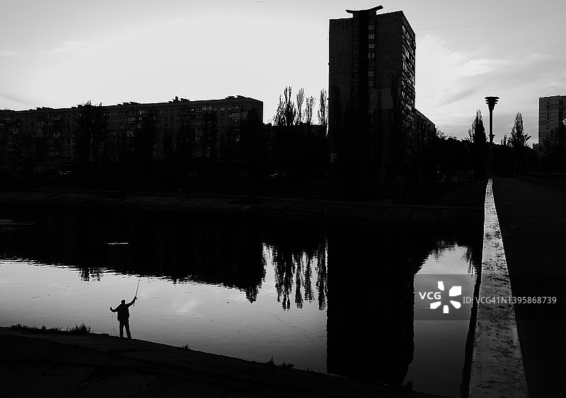 渔民在河堤上钓鱼的轮廓，背景是建筑物图片素材