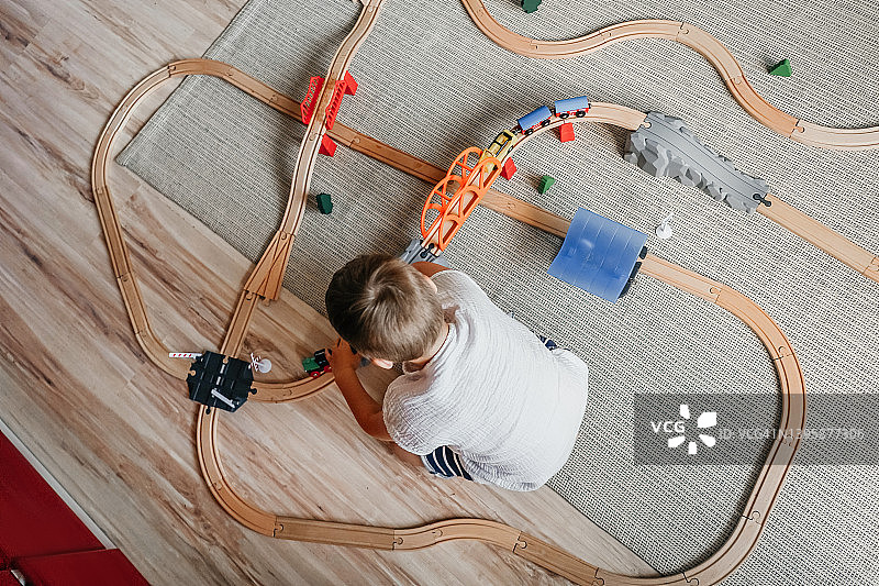 小男孩在家里的地板上玩铁木轨道图片素材