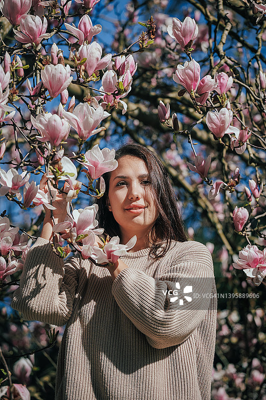 身穿针织毛衣的年轻女子在盛开的花园中散步，玉兰树图片素材