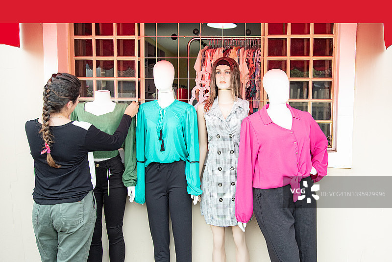 年轻女人在商店里从后面整理人体模型上的衣服图片素材