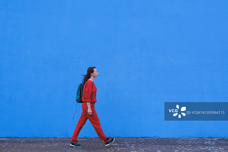 在蓝色背景墙前行走的女人，户外，旅行创意概念图片素材
