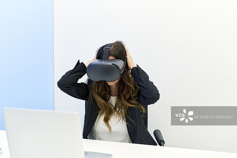商务场合成年女性使用VR眼镜坐在办公桌前图片素材