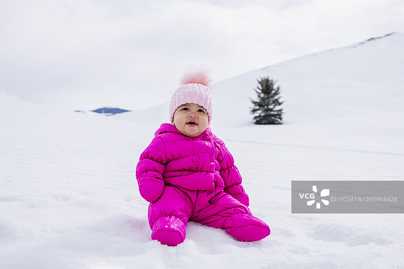 穿着粉色滑雪服坐在雪景中的女婴图片素材