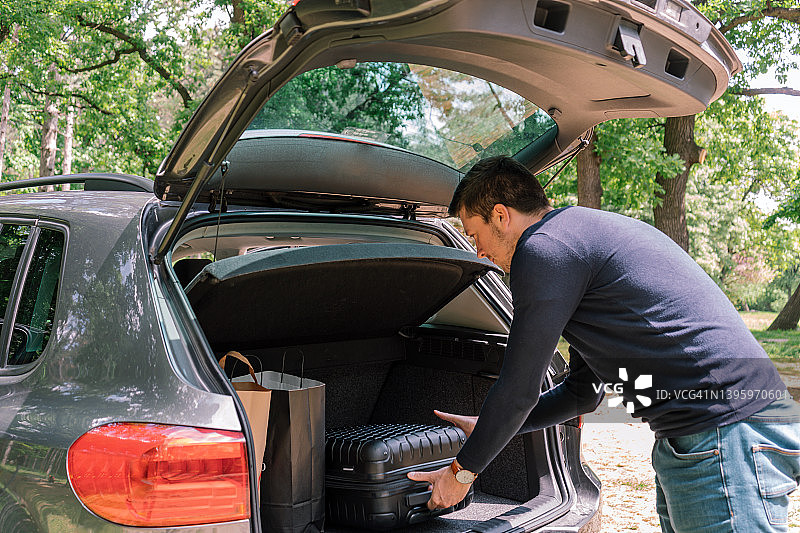 年轻男人在度假前将旅行包放入宽敞的汽车后备箱图片素材