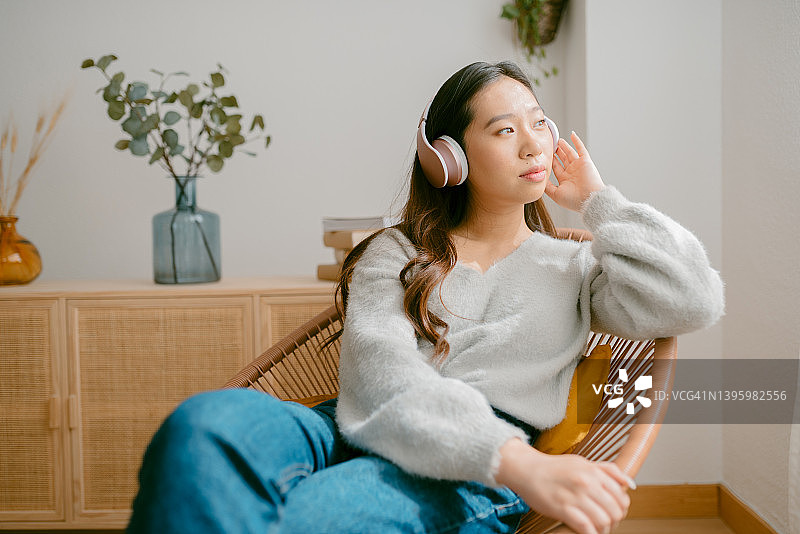 在椅子上边吃东西边戴着耳机听音乐的亚洲女人图片素材