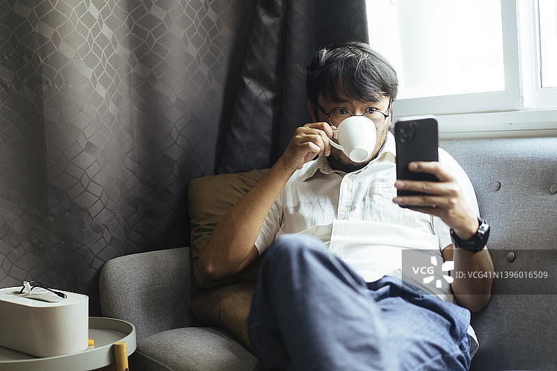 一位情绪积极的亚洲年轻自由职业者（数字游民）在家中使用手机和笔记本电脑工作，享受家庭生活图片素材