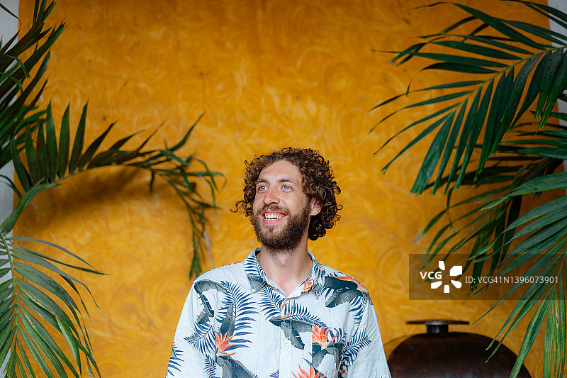 穿夏威夷衬衫的男人站在黄色墙壁的植物背景前图片素材