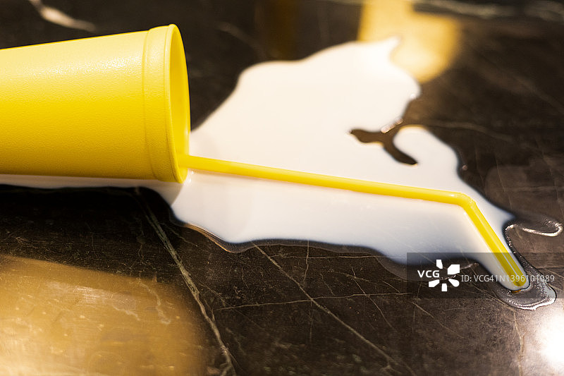 不要为洒出的牛奶哭泣：明黄色杯子和吸管被打翻在柜台上，牛奶飞溅（侧视图）图片素材
