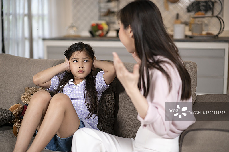愤怒的母亲冲着坐在沙发上的女儿喊叫图片素材