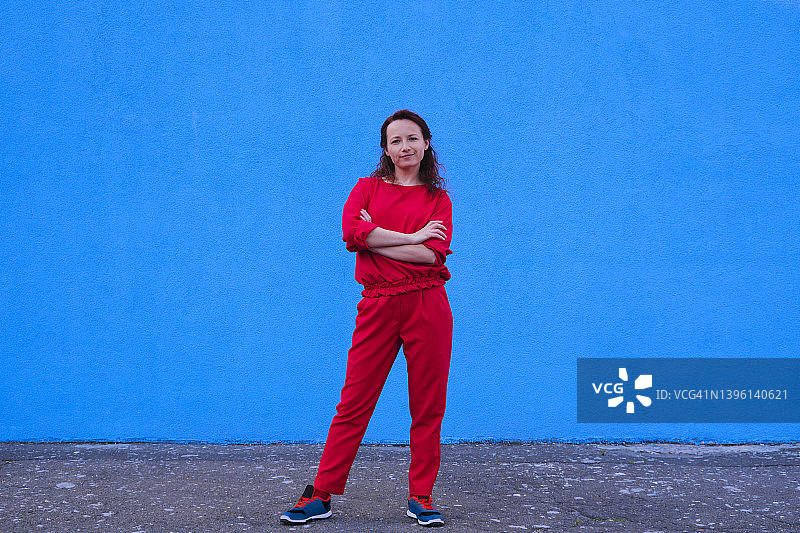 穿着红色休闲风格服装，双手放在胸前的女人。鲜艳的蓝色墙壁背景图片素材