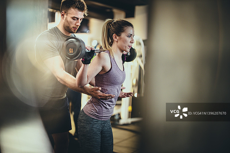 在健身房与教练一起进行重量训练的健壮女人图片素材