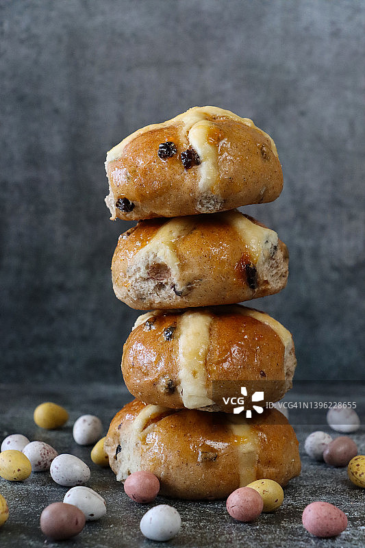 一堆新鲜出炉的自制复活节十字面包的特写，周围环绕着斑点糖果涂层巧克力迷你复活节彩蛋，灰色的背景，家庭烘焙概念，前景聚焦图片素材