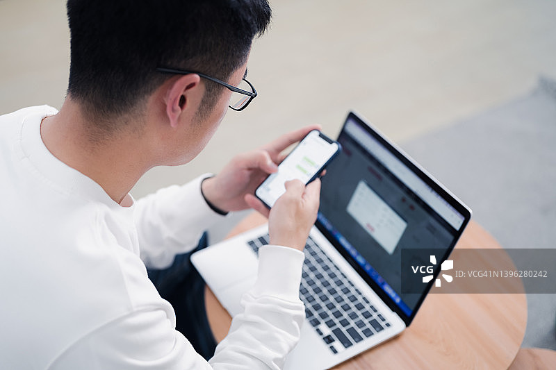 年轻男子在家使用电脑和智能手机的背影图片素材