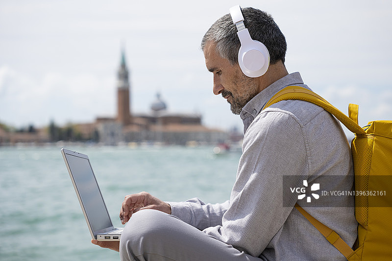 在威尼斯度假的男人听着音乐用笔记本电脑工作。图片素材