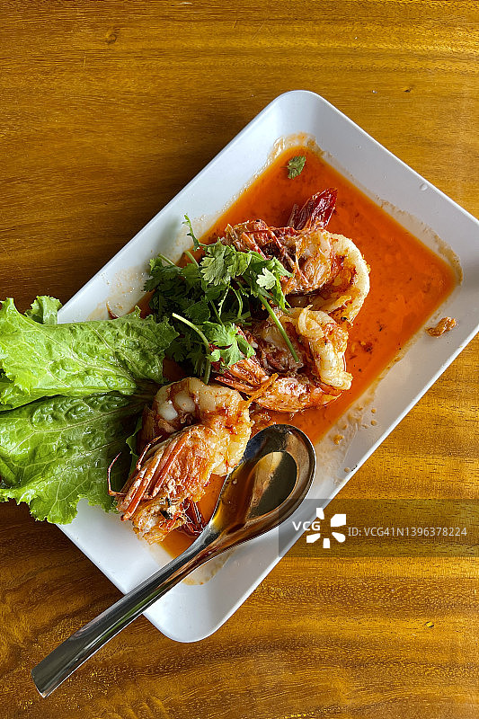 泰式海鲜背景——白色盘子上用辛辣酱汁炒巨型虎虾，木桌顶视图图片素材