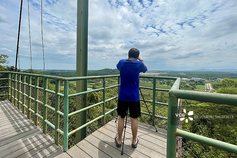 身穿蓝色T恤和短裤的男游客在山顶观景点拍摄罗勇府的风景，考博观景点图片素材