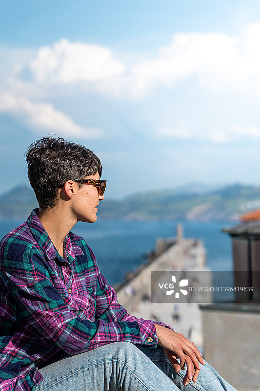 以美丽风景灯塔和海港为背景，戴着太阳镜的微笑的短发年轻女子肖像图片素材