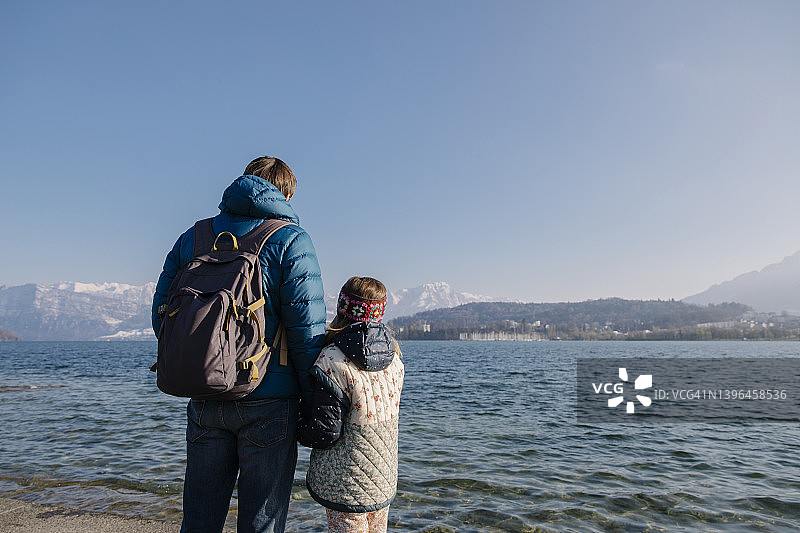 父亲背着背包和女儿站在湖边图片素材