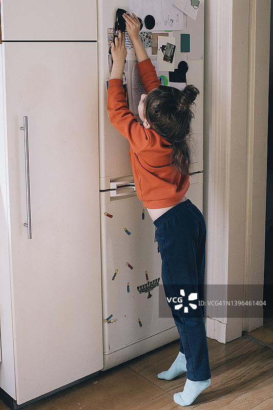 女孩在家把磁铁贴在冰箱门上全身照图片素材