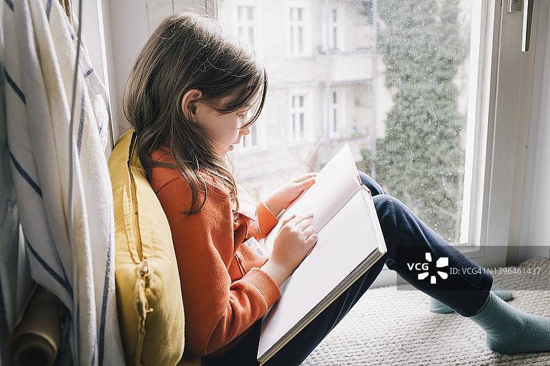 女孩坐在窗台上看书的侧面视角图片素材