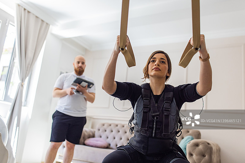 健身教练用平板电脑控制EMS设备，指导女客户哑铃训练图片素材