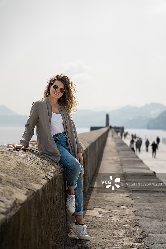 戴墨镜靠在海边防波堤上的年轻金发女子肖像图片素材