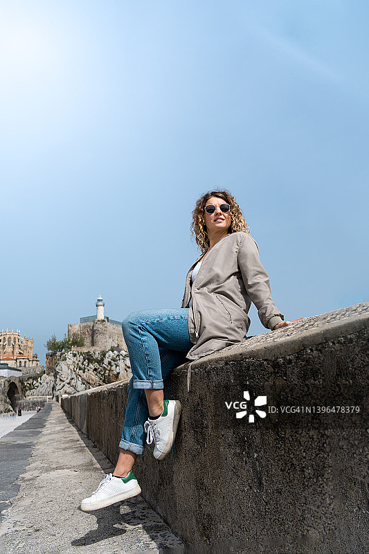 戴墨镜靠在海边防波堤上的年轻金发女子肖像图片素材