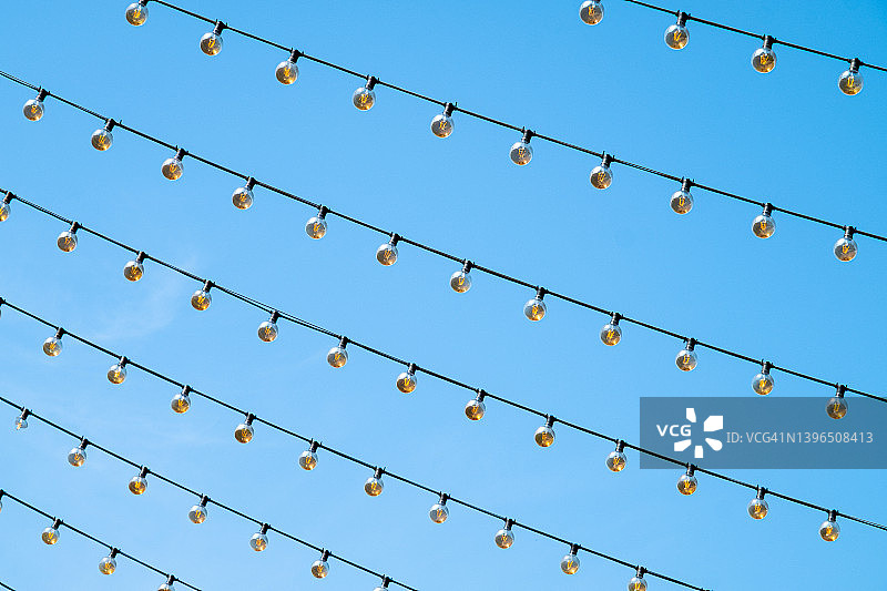 户外悬挂一排灯泡花环，蓝色天空背景下的装饰灯笼，留白区域图片素材