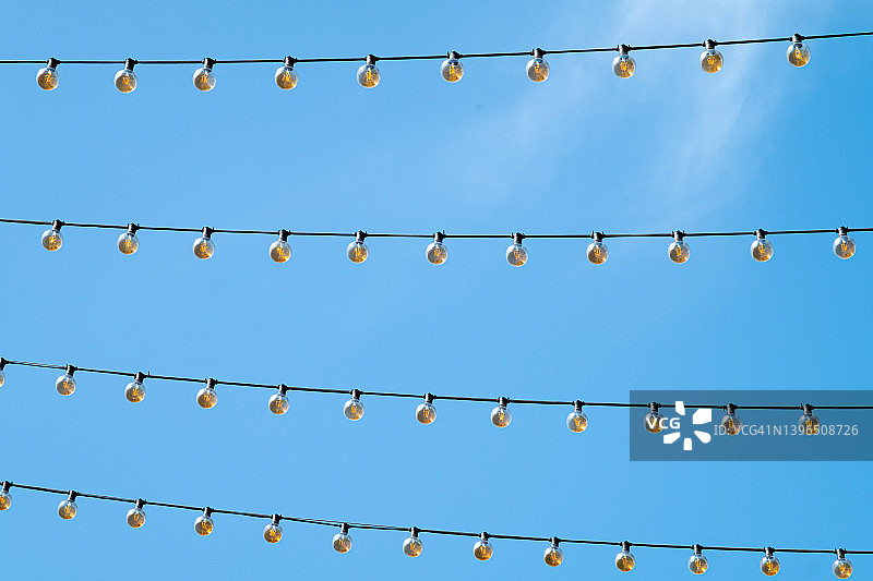 户外悬挂一排灯泡花环，蓝色天空背景下的装饰灯笼，留白区域图片素材