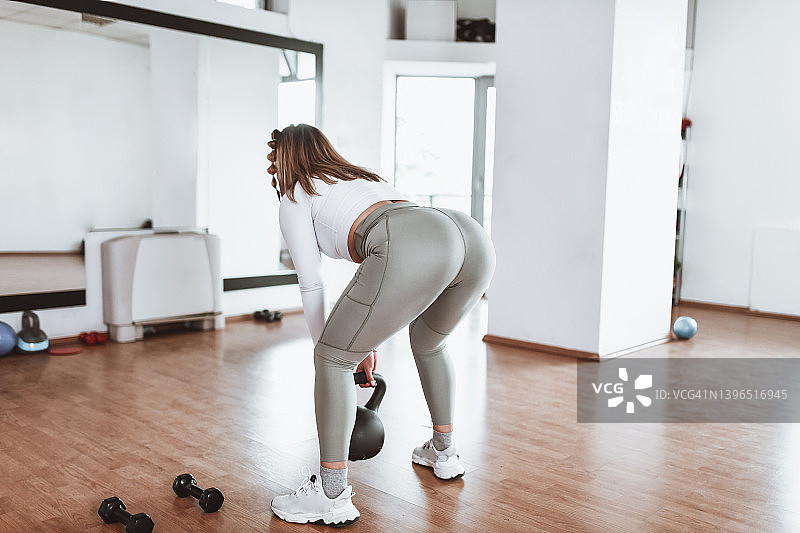穿着运动服的女运动员正在改进壶铃摆动的后视图图片素材