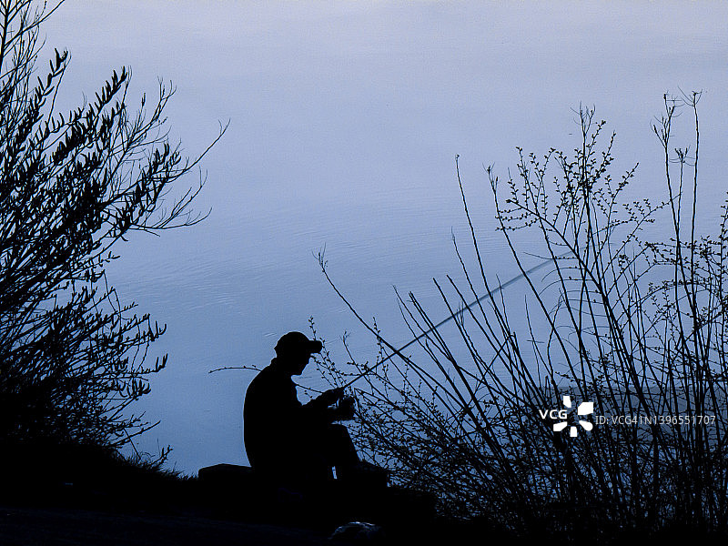 渔夫在河边植物旁钓鱼的轮廓图片素材