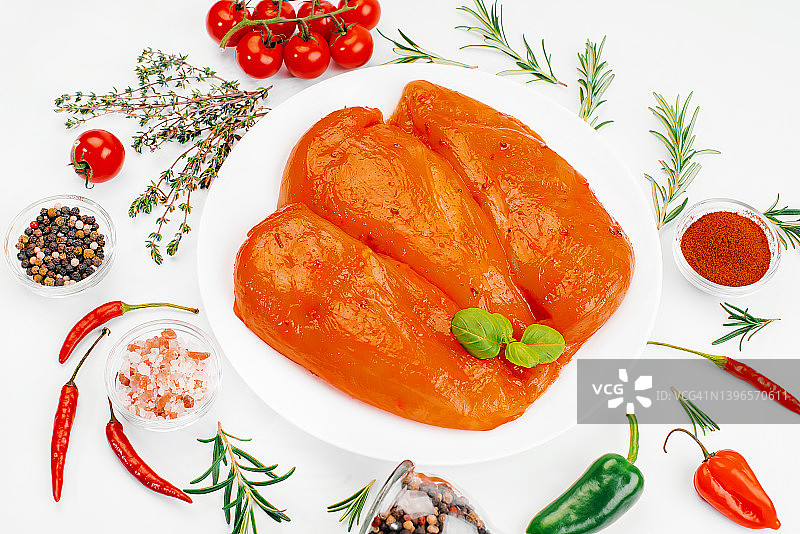 白色盘子上红酱生腌鸡柳，白色背景，配有烹饪用香料。膳食鸡肉。生产品。用于烤制的鲜腌鸡肉。膳食肉。图片素材