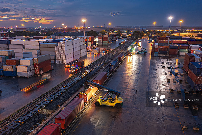 黄昏时分，叉车将集装箱装载到货运列车上，用于商业物流、进出口运输或货运的航拍图。图片素材