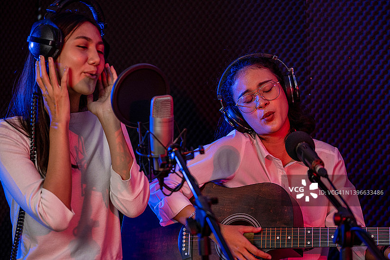 在专业录音棚录制歌曲时对着电容麦克风二重唱的快乐年轻女子肖像图片素材