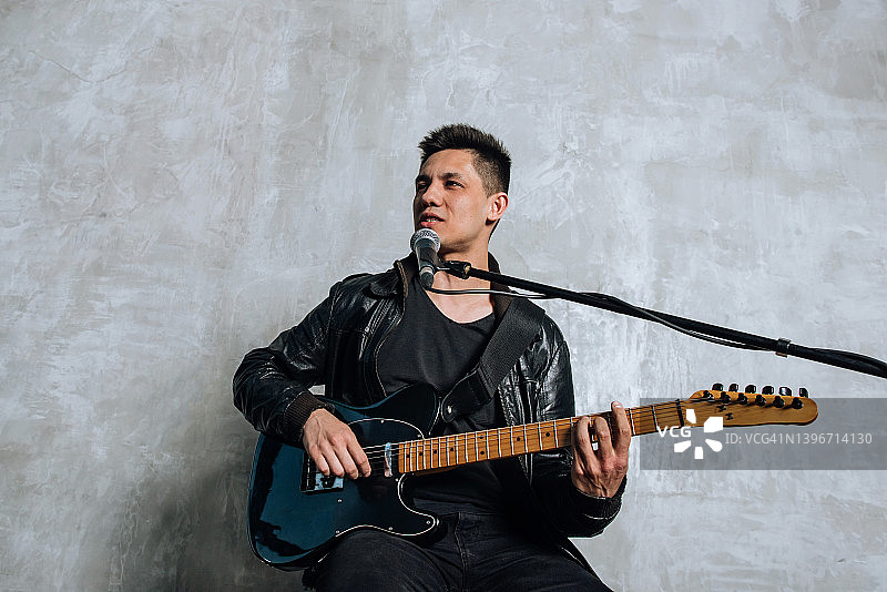 男吉他手弹吉他唱歌，对着麦克风演唱歌曲图片素材