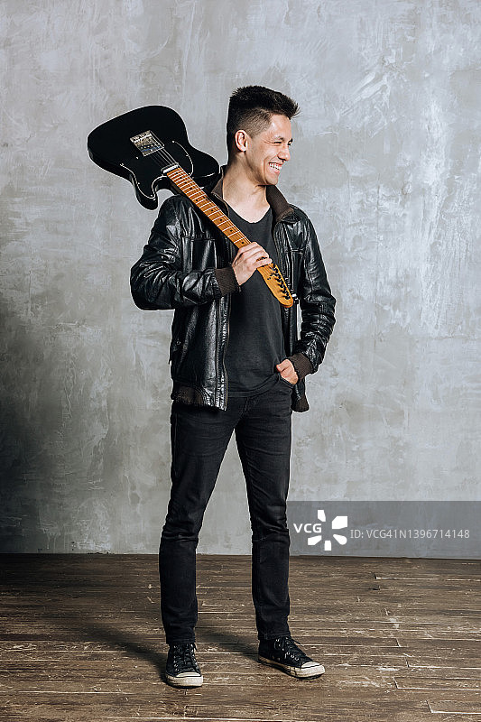 快乐的亚洲音乐家吉他手肩扛吉他在工作室里笑着图片素材