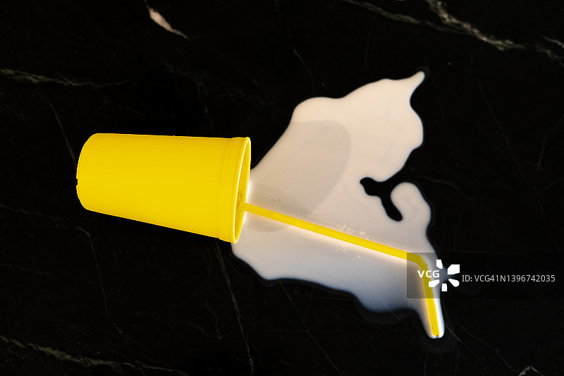 不要为洒出的牛奶哭泣：明黄色杯子和吸管倒在柜台上，牛奶飞溅图片素材