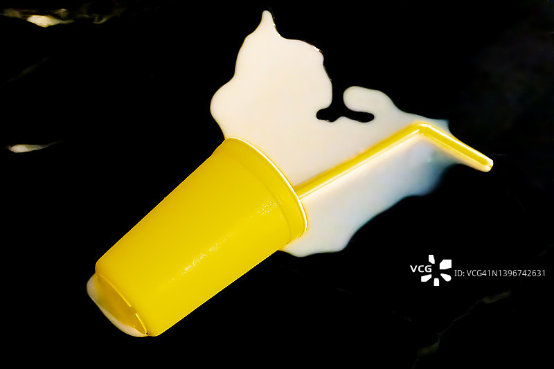 不要为洒出的牛奶哭泣：明黄色杯子和吸管倒在柜台上，牛奶飞溅图片素材