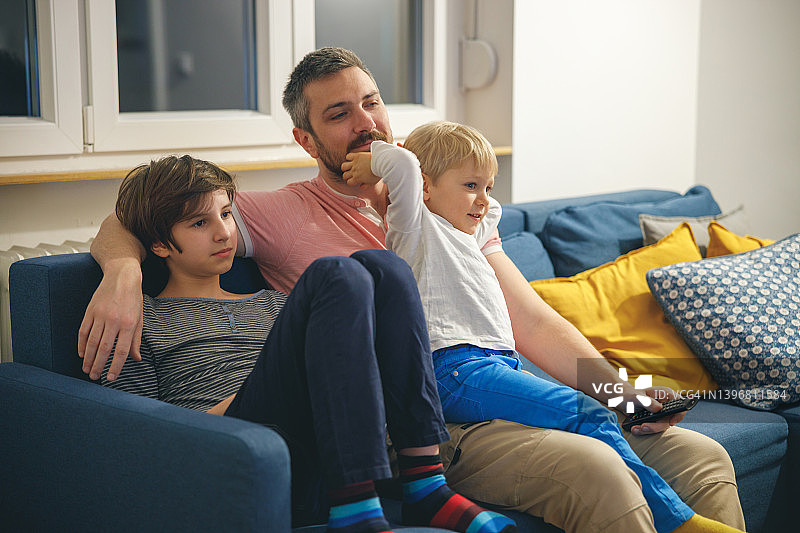 父亲在父亲节与儿子们在家中沙发上享受电影之夜图片素材