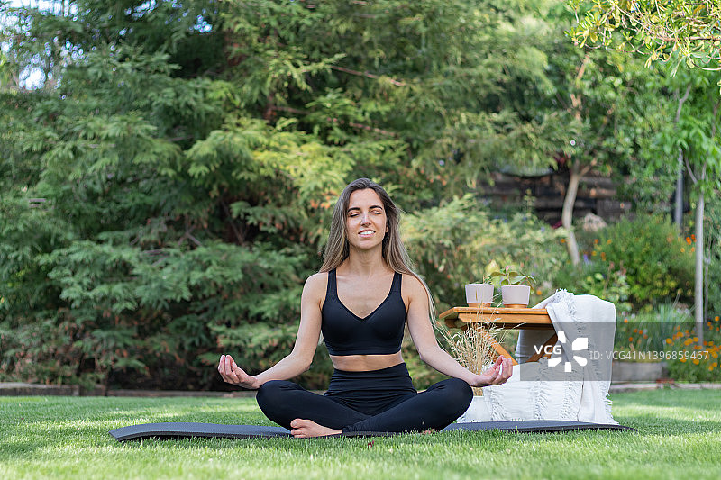 年轻女子在花园里练习莲花式瑜伽（正面视角）图片素材