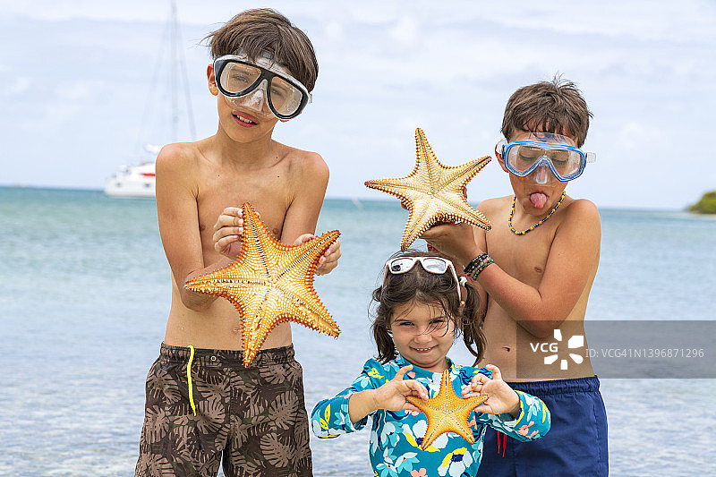 三个快乐的孩子在海滩上拿着海星图片素材