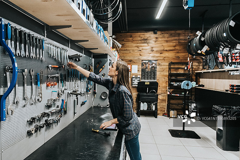 年轻女人在车间里从工具架上取工具图片素材