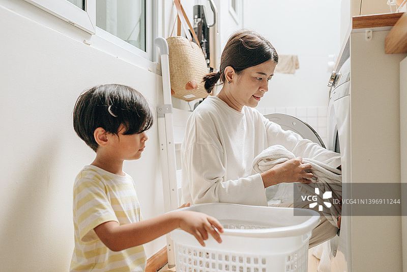 男孩和年轻母亲一起把衣服放进洗衣机图片素材