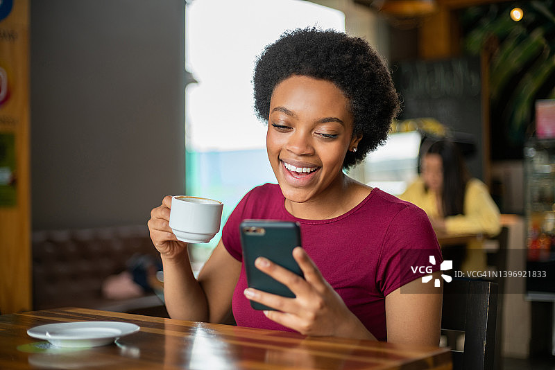 快乐的女人在咖啡馆喝咖啡时看手机图片素材